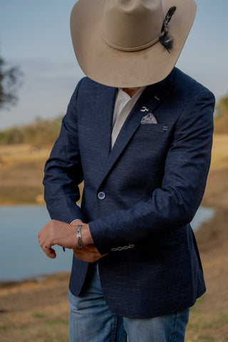 Person wearing a navy blazer and beige hat outdoors by a body of water.