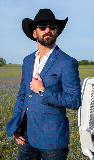 Man in a blue suit and cowboy hat standing in a field with a clear sky.