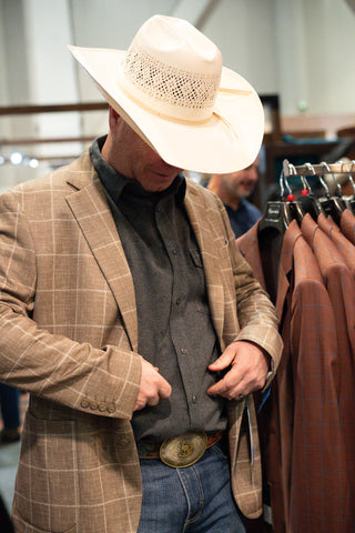 Cowboy shopping for the right western blazer that can be worn with cowboy hat and boots and jeans. This is a tan with plaid pattern on front. Cowboy is wearing a straw hat. 