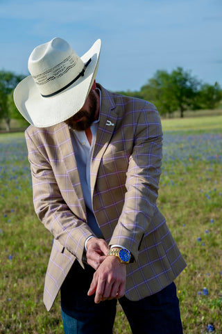 Man wearing a plaid blazer and white cowboy hat in a field with blue flowers.