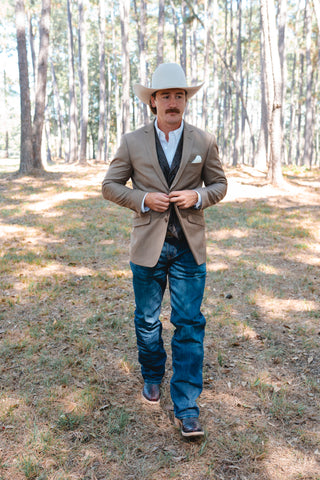Man in cowboy hat and western attire standing in a forested area